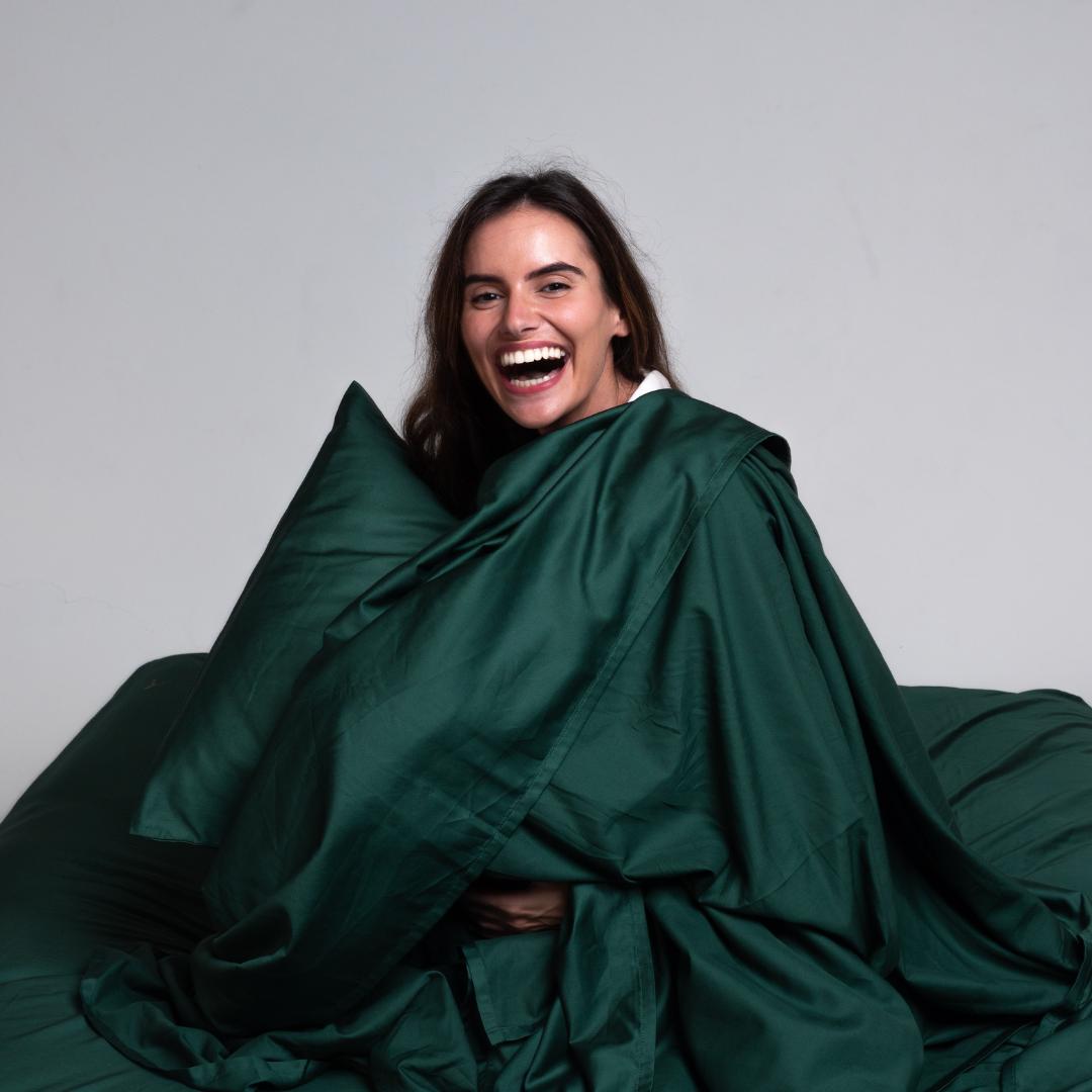 Woman smiling while wrapped in green TLC bamboo-cotton sheets