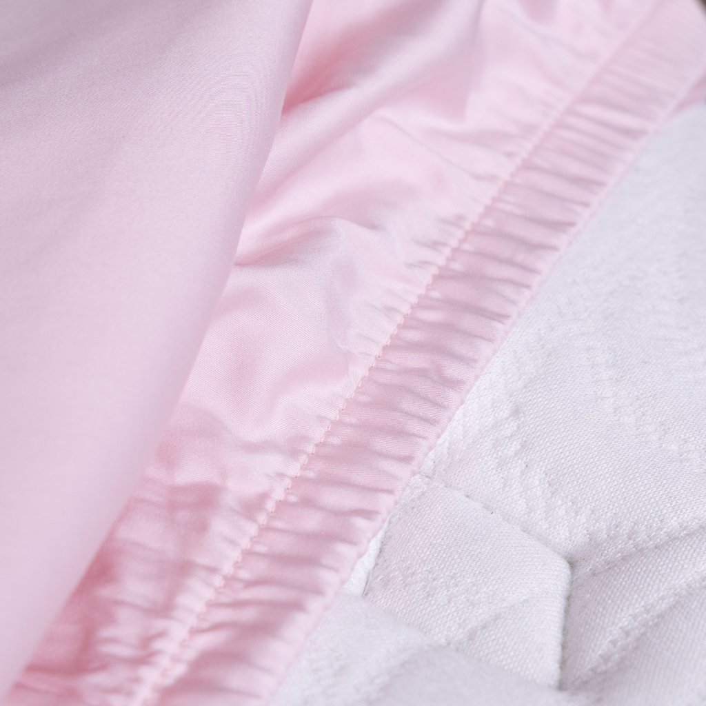 Close-up of The Lad Collective blush pink bamboo cotton blend fitted sheet with elastic edge securely hugging a mattress, showcasing premium stitching and snug fit.