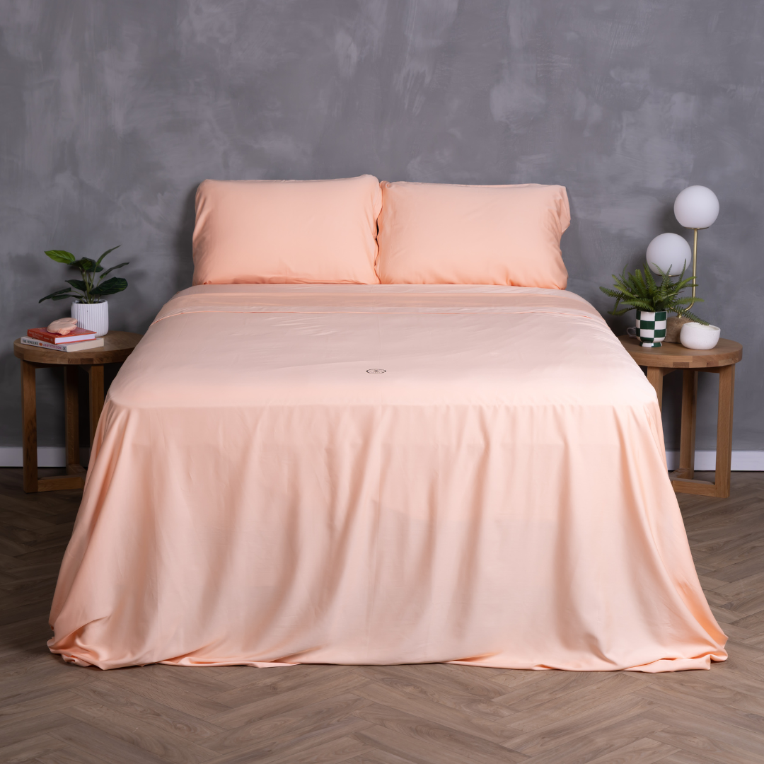 Peach-coloured bedding set on a neatly made bed with matching pillowcases and fitted sheet – breathable, buttery-soft sheets styled in a modern bedroom with timber bedside tables and indoor plants.