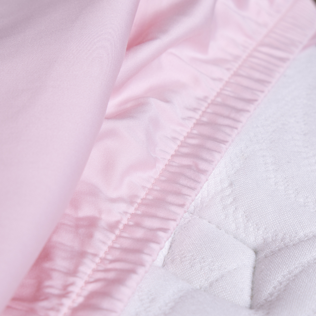 Close-up of The Lad Collective blush pink bamboo cotton blend fitted sheet with elastic edge securely hugging a mattress, showcasing premium stitching and snug fit.