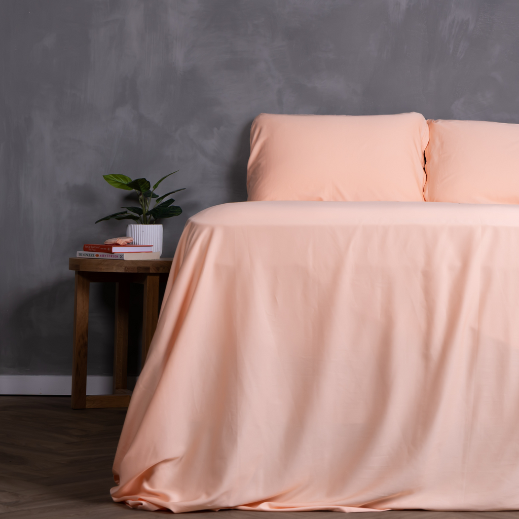 Peach-coloured bedding set on a neatly made bed with matching pillowcases and fitted sheet – breathable, buttery-soft sheets styled in a modern bedroom with timber bedside tables and indoor plants.