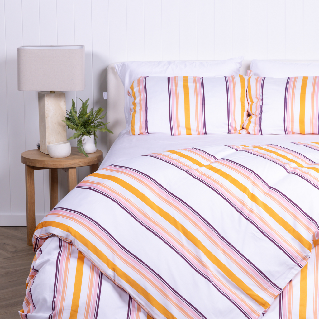 White, yellow and burnt orange striped duvet cover set with matching pillowcases, styled on modern bed with wooden bedside tables.