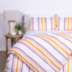White, yellow and burnt orange striped duvet cover set with matching pillowcases, styled on modern bed with wooden bedside tables.