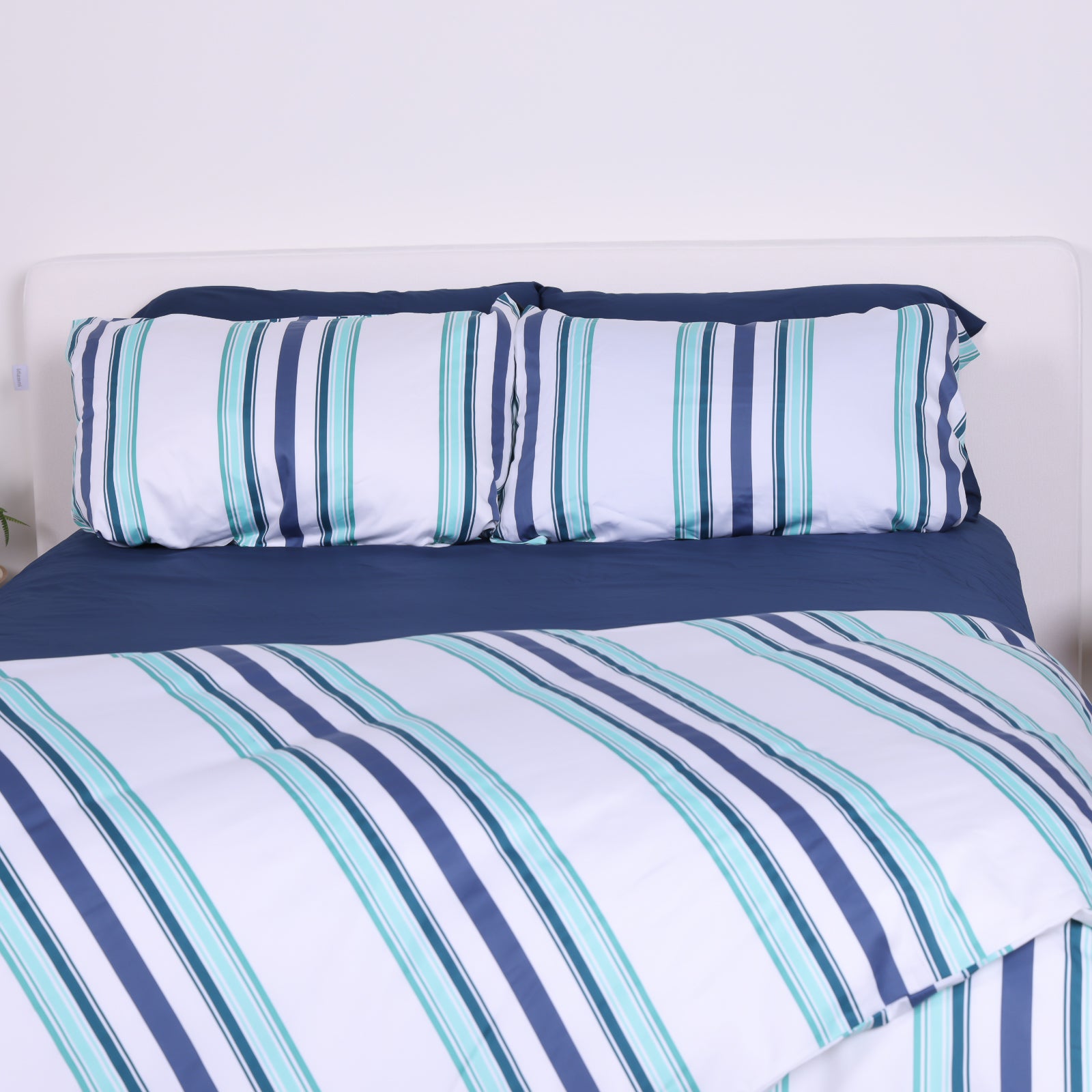 White, blue and teal striped duvet cover set with matching pillowcases and navy fitted sheet on modern bed.