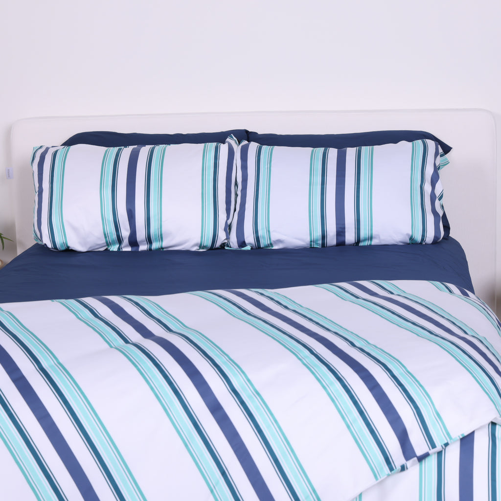 White, blue and teal striped duvet cover set with matching pillowcases and navy fitted sheet on modern bed.