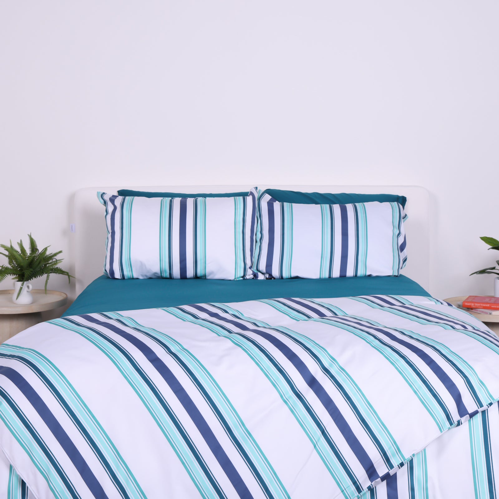 White, blue and teal striped duvet cover set with matching pillowcases and teal fitted sheet, styled on modern bed.