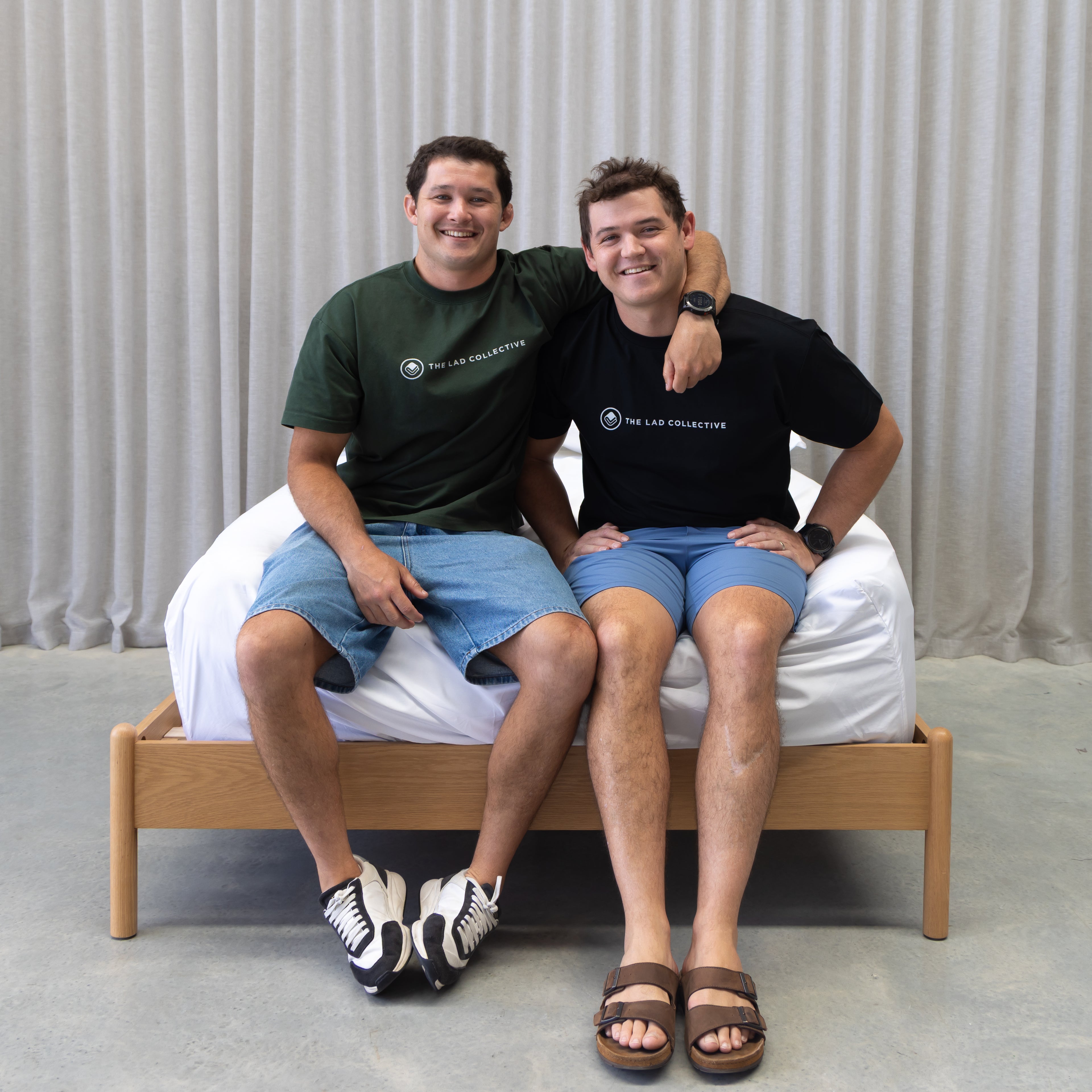 Two men sitting on a bed with a plain background