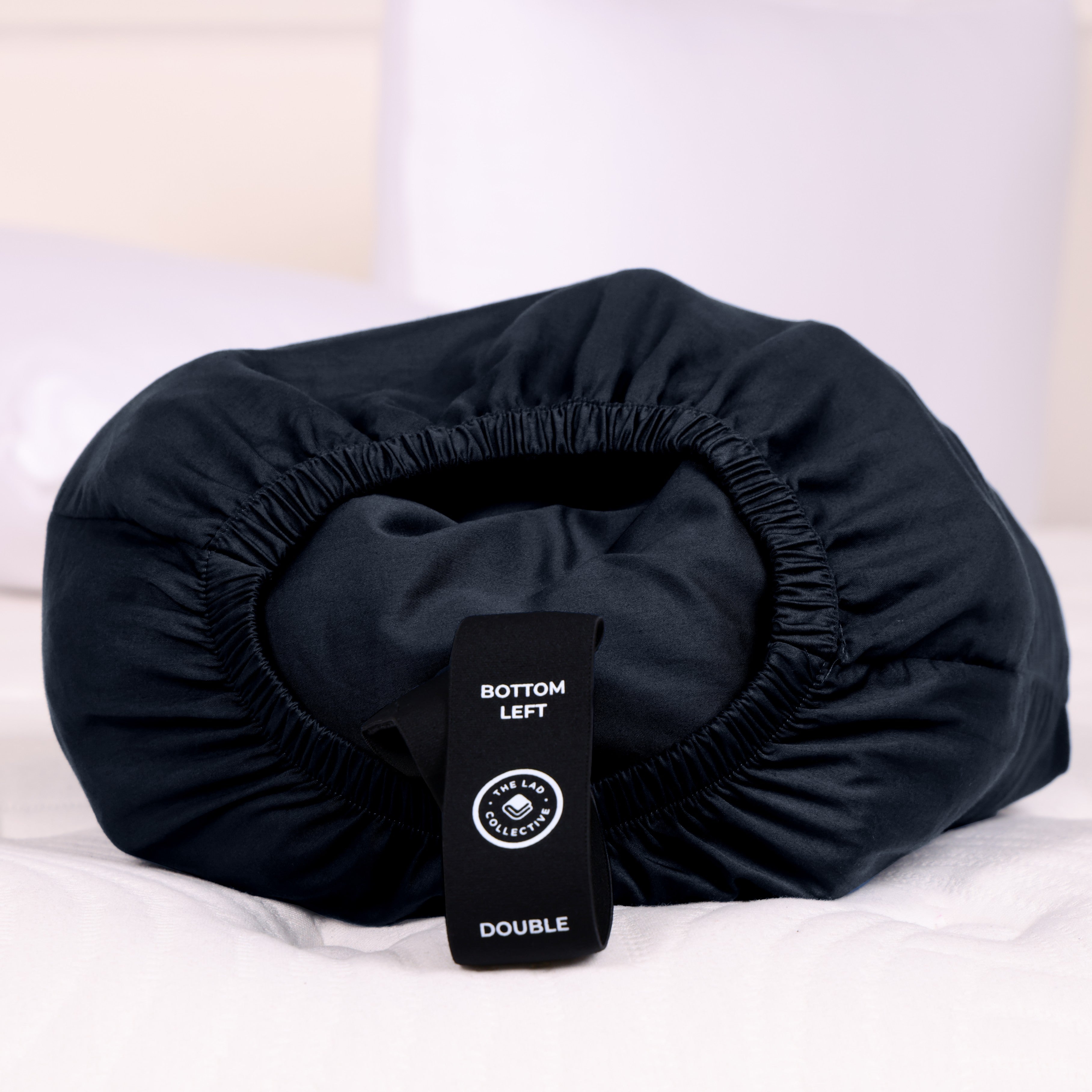 The Lad Collective black fitted sheet neatly packed into its signature Joey Pouch with labeled “Top Left” and “Double” tag, showcasing convenient storage and easy bed-making system.