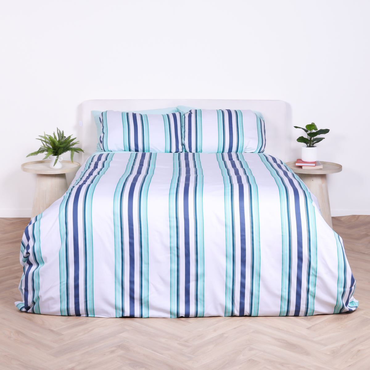 White, blue and teal striped duvet cover set with matching pillowcases, styled on bed with modern bedside tables.