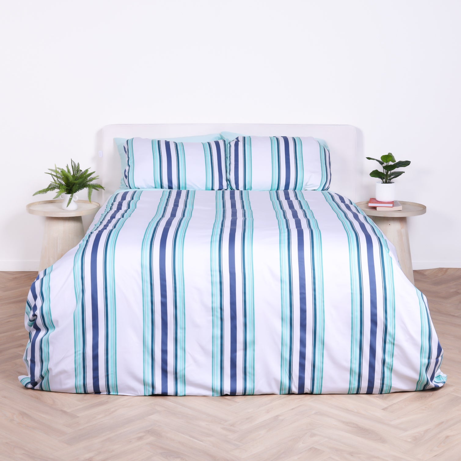 White, blue and teal striped duvet cover set with matching pillowcases, styled on bed with modern bedside tables.