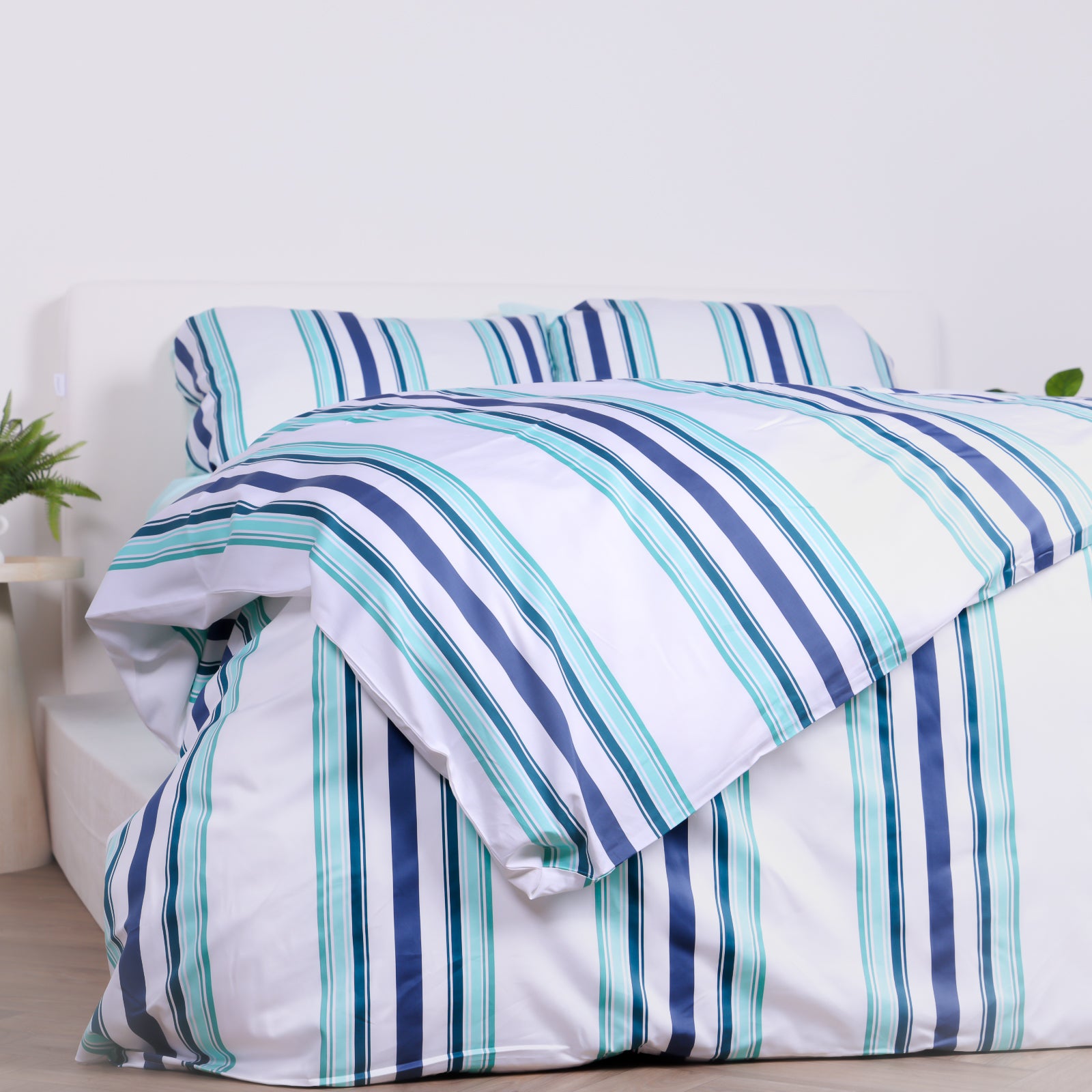 White, blue and teal striped duvet cover set with matching pillowcases, styled on bed with modern bedside tables.