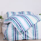 White, blue and teal striped duvet cover set with matching pillowcases, styled on bed with modern bedside tables.