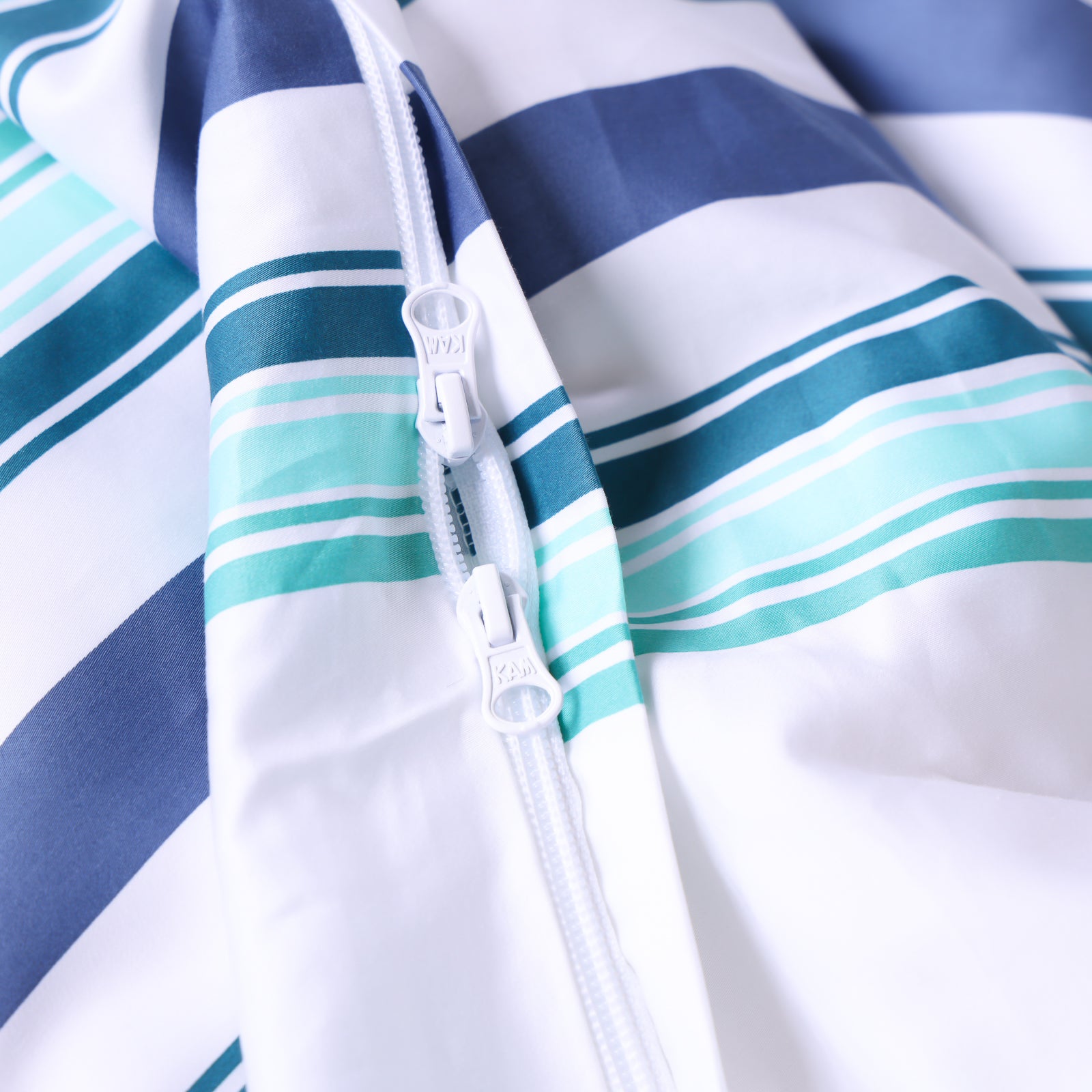 Close-up of invisible zipper closure at base of white, blue and teal striped duvet cover.