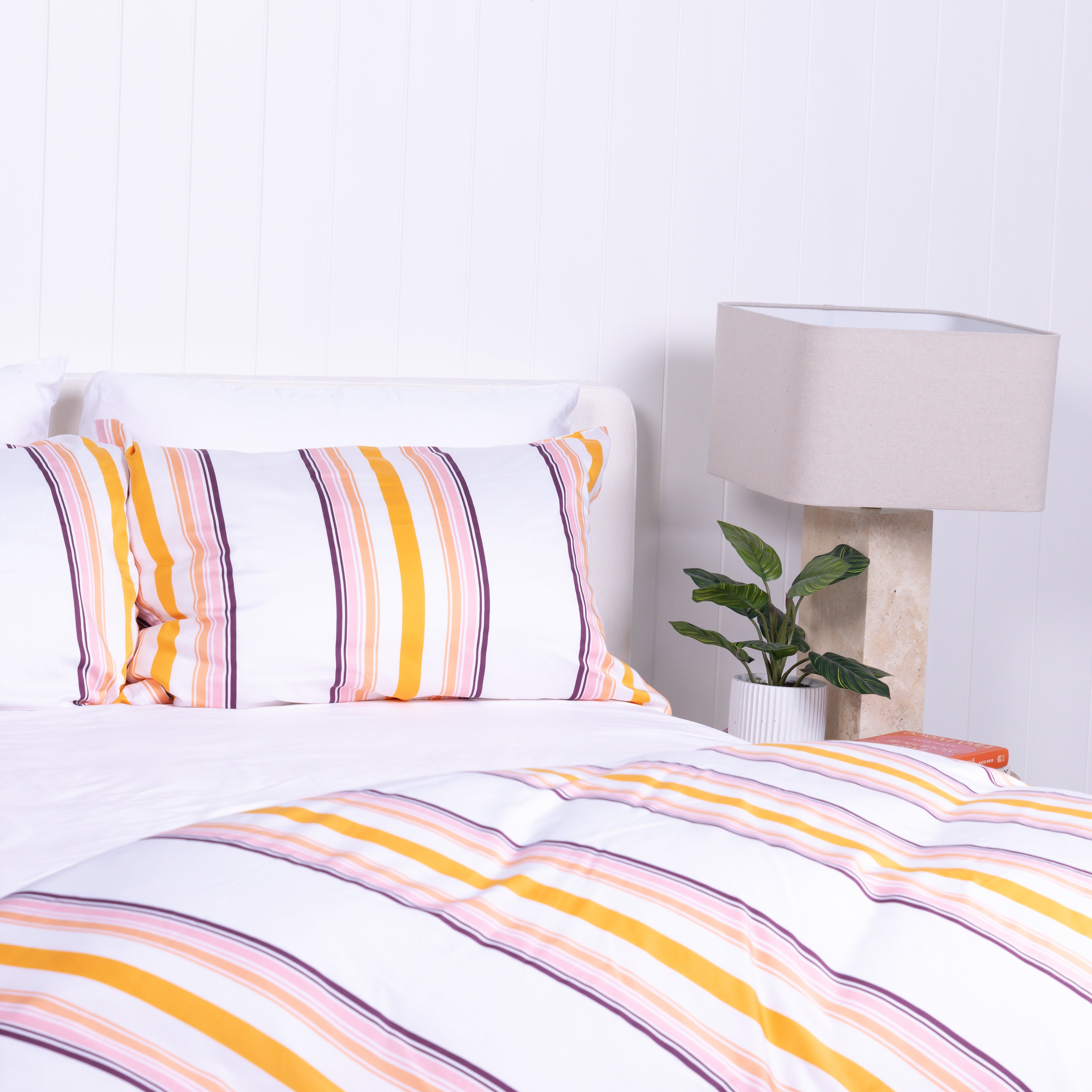 White, yellow and burnt orange striped duvet cover set with matching pillowcases, styled on modern bed with wooden bedside tables.