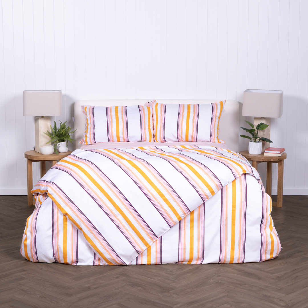 White, yellow and burnt orange striped duvet cover set with matching pillowcases, styled on modern bed with wooden bedside tables.