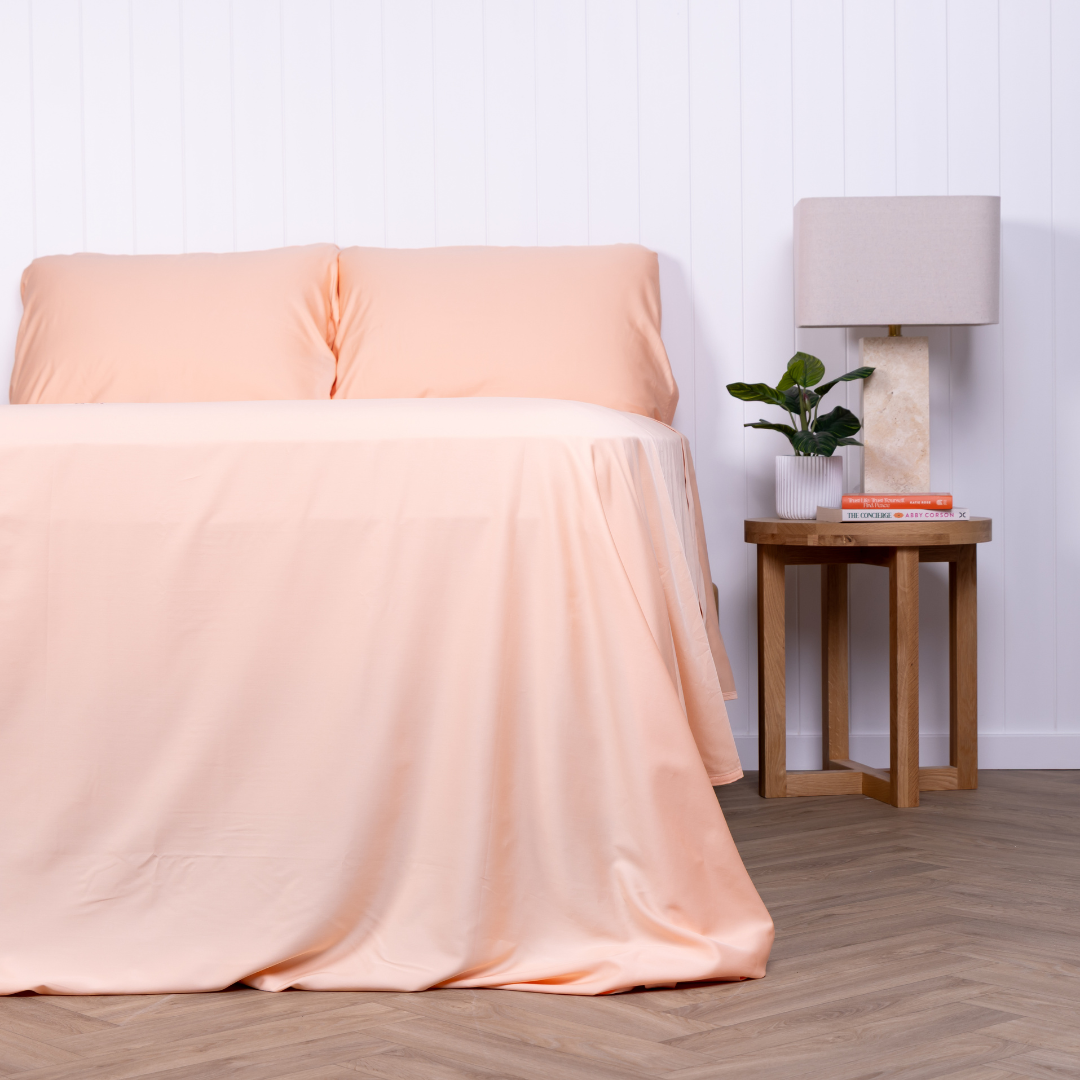 Peach-coloured bedding set on a neatly made bed with matching pillowcases and fitted sheet – breathable, buttery-soft sheets styled in a modern bedroom with timber bedside tables and indoor plants.