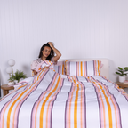 Woman sitting in bed with white, yellow, pink and plum striped duvet cover set and matching pillowcases.