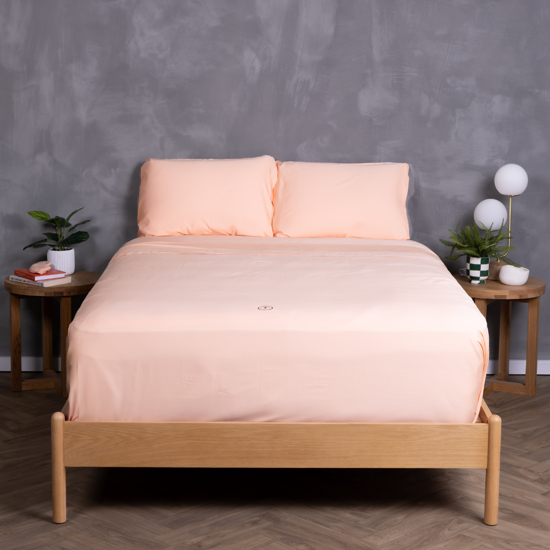 Peach sheet set neatly styled on a timber bed frame with matching pillowcases – breathable, ultra-soft bedding in a modern bedroom with grey feature wall, timber bedside tables and indoor plants.
