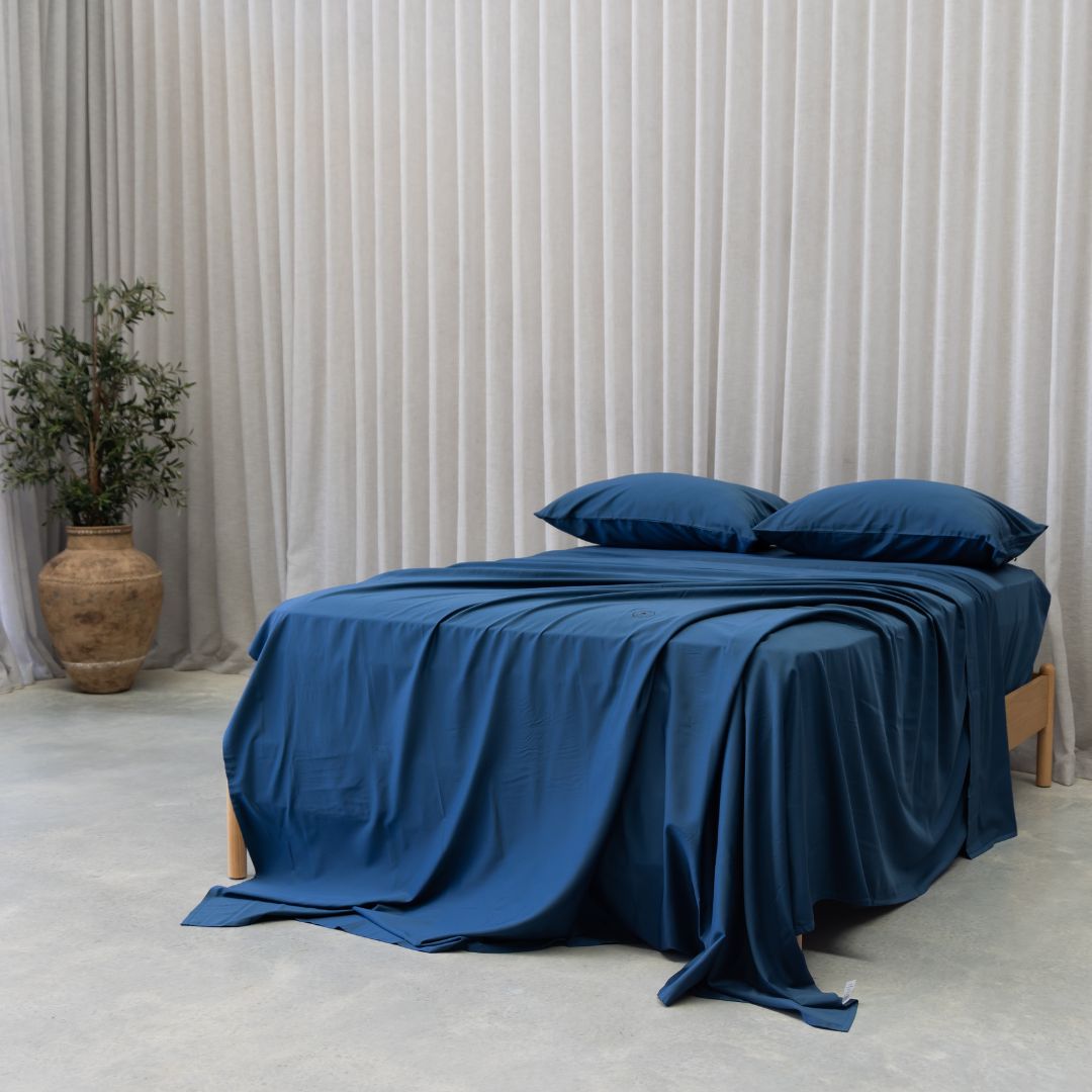 Blue bedspread on a bed with pillows against a neutral background