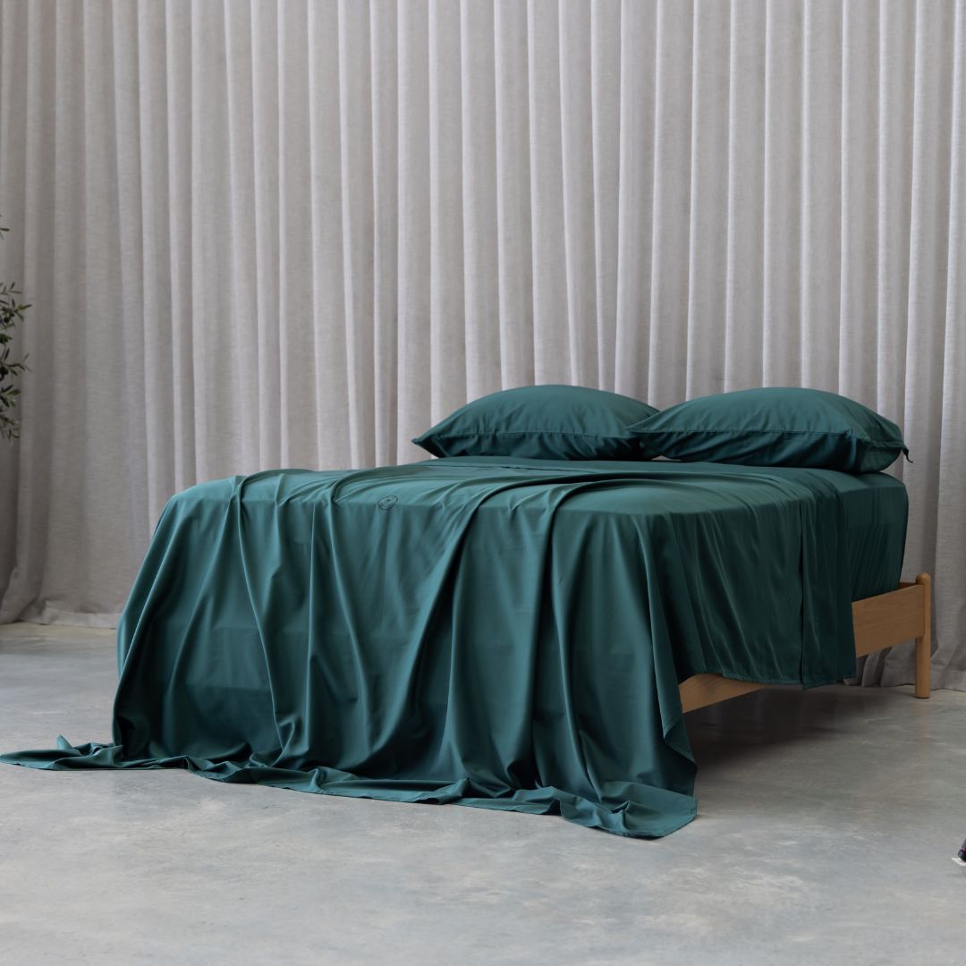 Deep green bamboo sheet set on queen bed in minimalist bedroom.