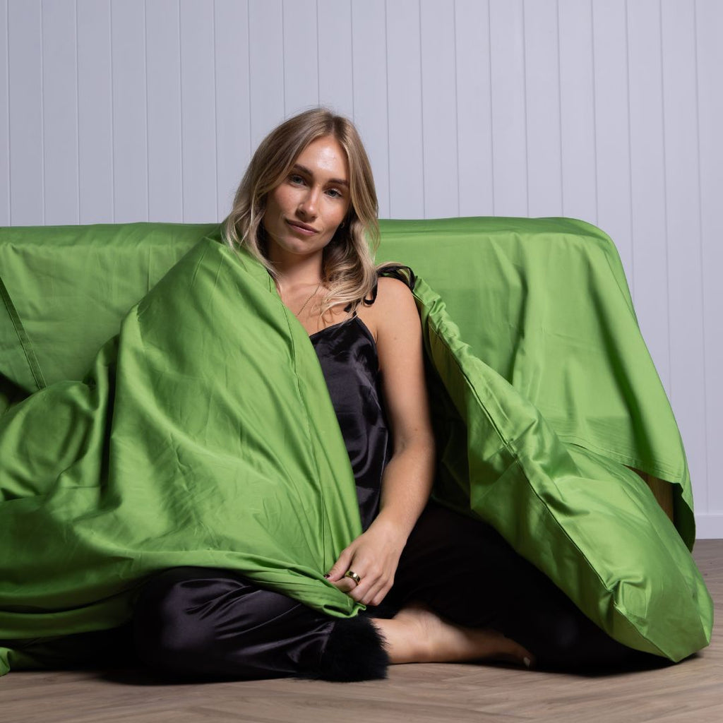 Woman wrapped in green Colorado duvet on floor, relaxed vibe. 