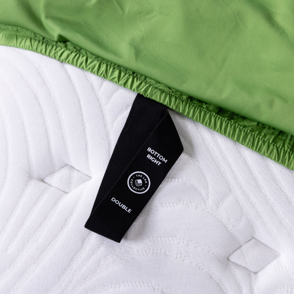 Macro view of TLC labeled loop on green fitted sheet against white mattress.