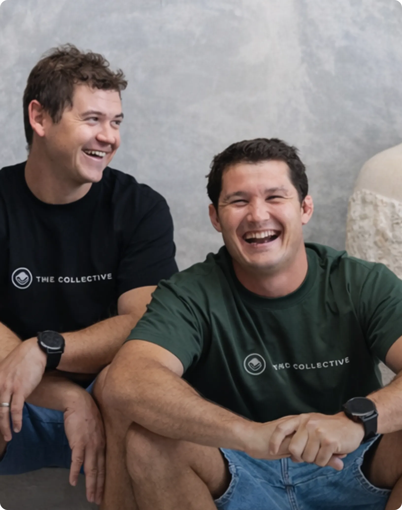 Two men sitting together, both wearing black t-shirts with 'The Collective' logo.