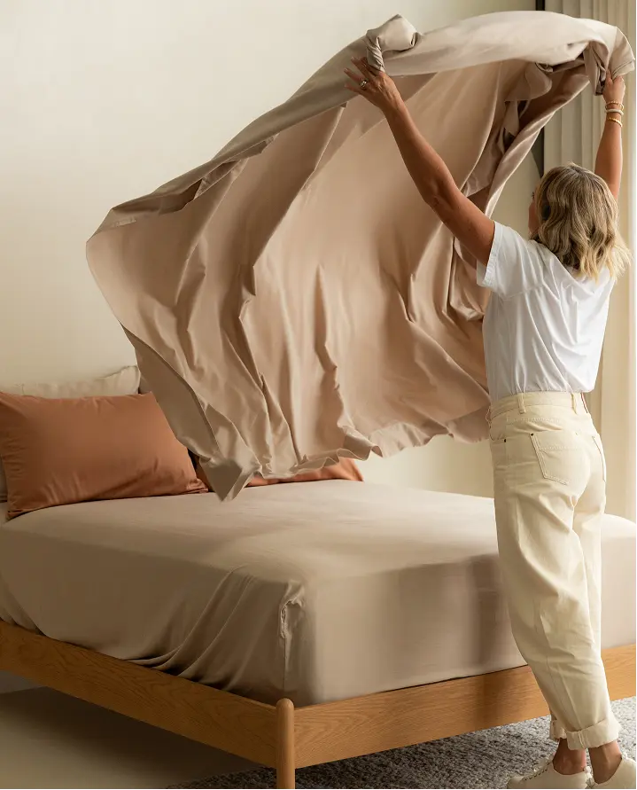 A woman lifting a flat sheet while making a bed