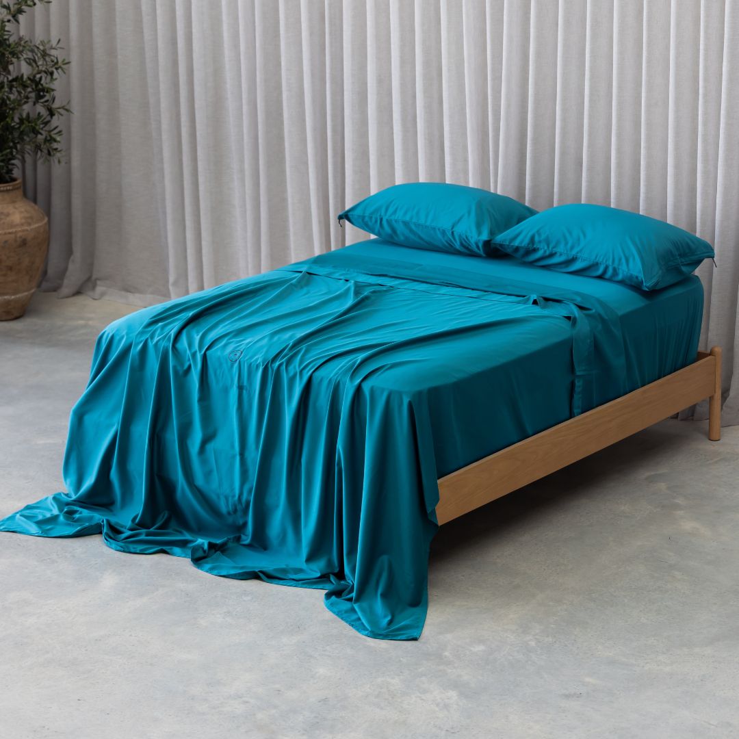 Teal bedspread and pillows on a wooden bed against a neutral background