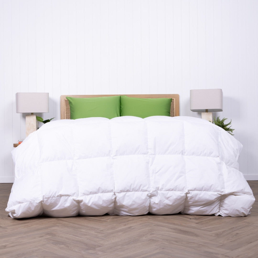 White comforter on a bed with green pillows and two lamps in a room.
