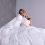 Woman lying under a white comforter against a gray wall.