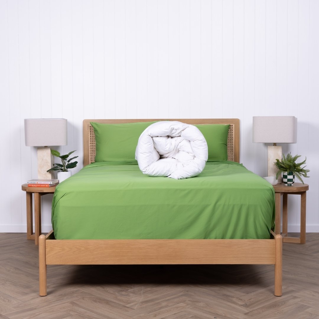 Bed with green bedding and wooden frame in a room with lamps and plants.