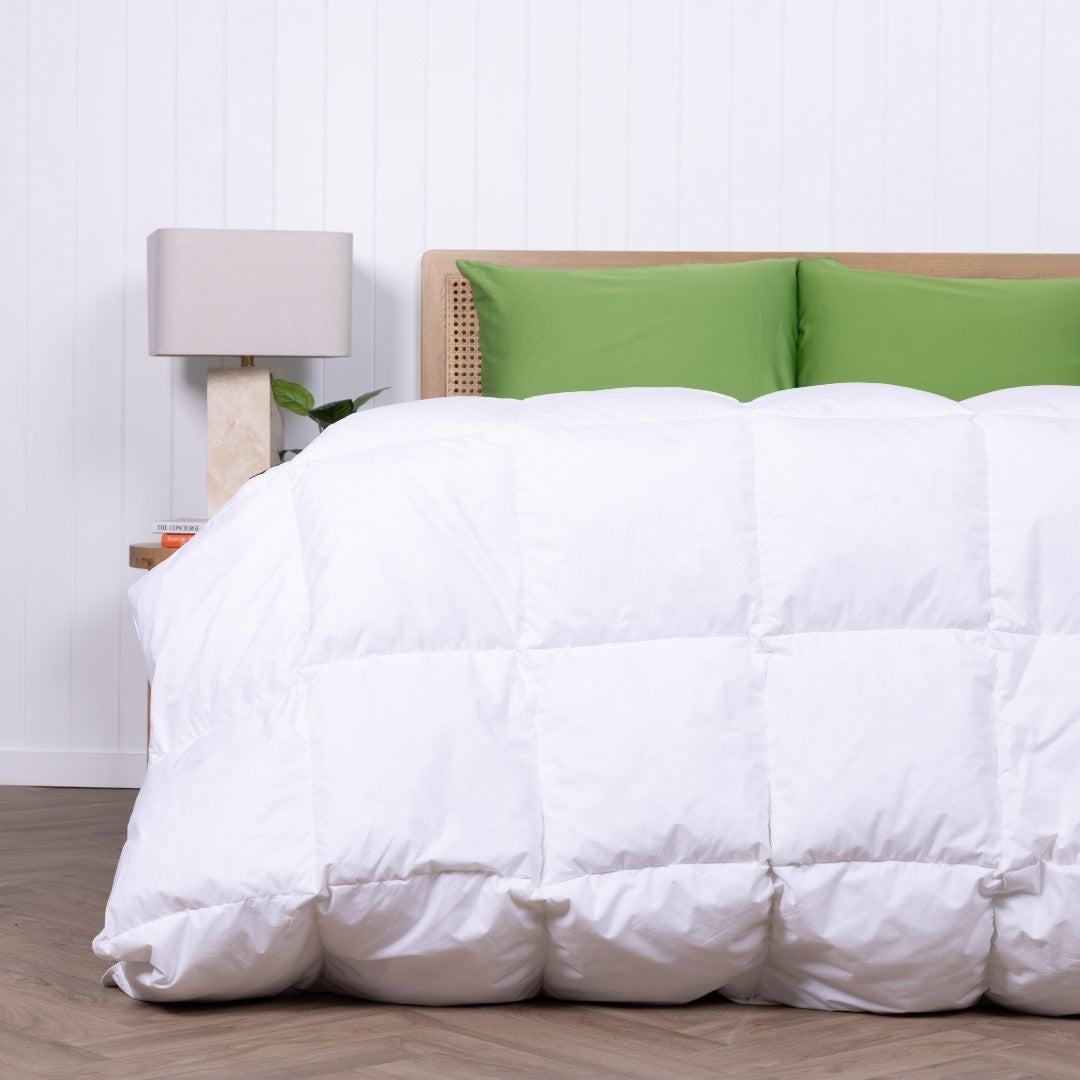 White comforter on a bed with green pillows and a lamp in the background.