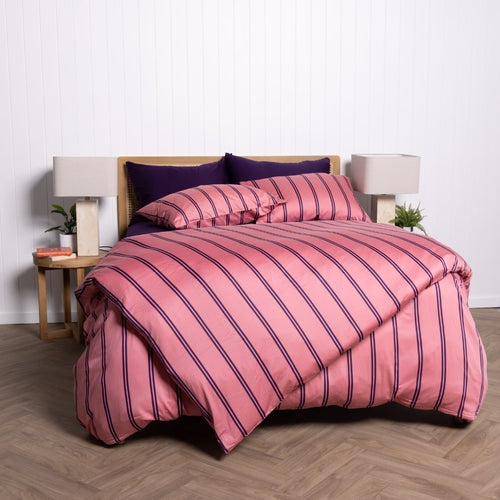 Bed with pink and purple striped bedding in a room with lamps and a plant.