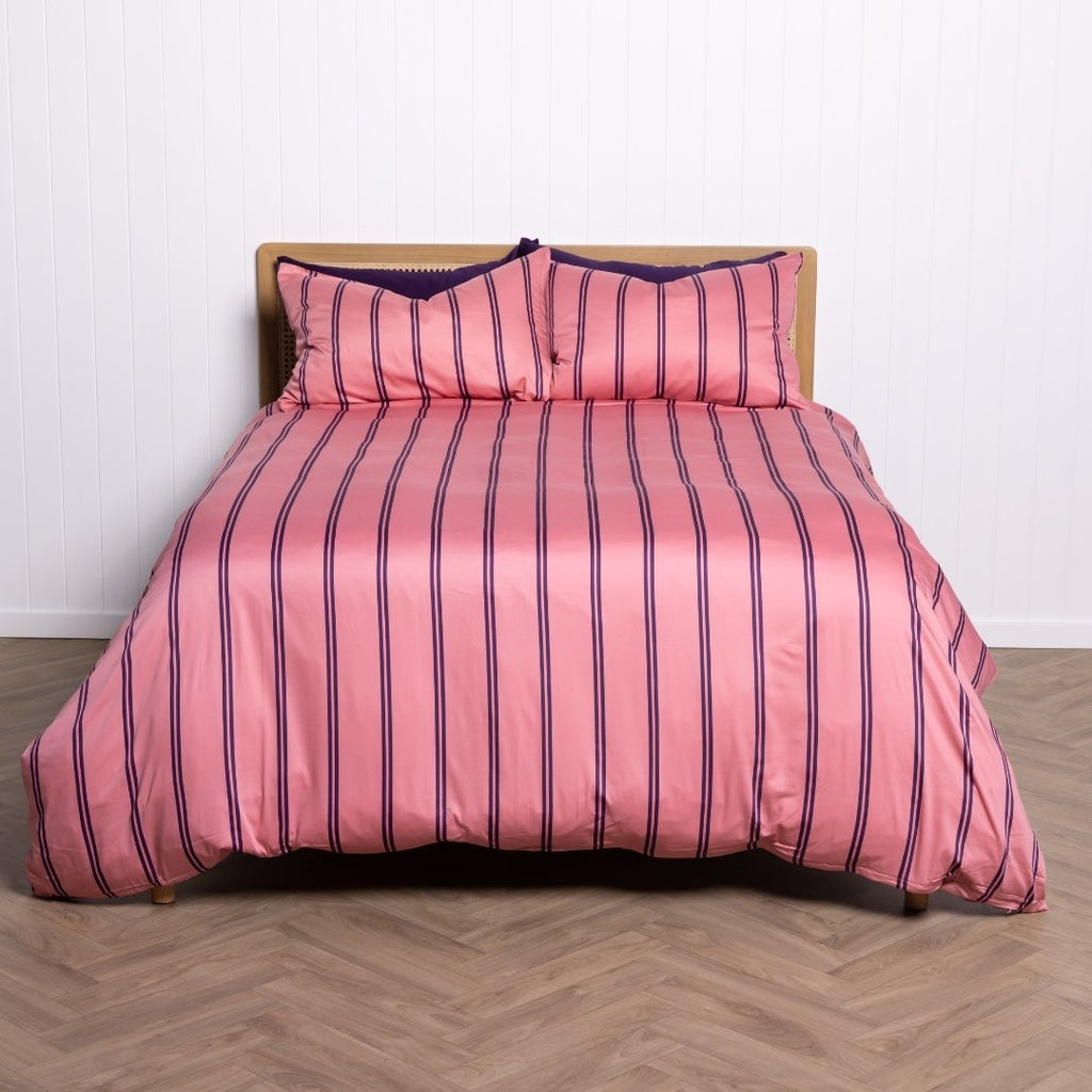 Pink striped bedspread with matching pillows on a wooden bed frame against a white wall.