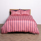 Pink striped bedspread with matching pillows on a wooden bed frame against a white wall.