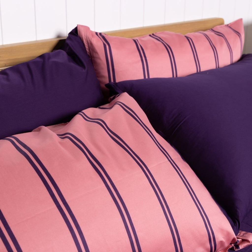 Pink and purple striped pillows on a bed with a white wall background