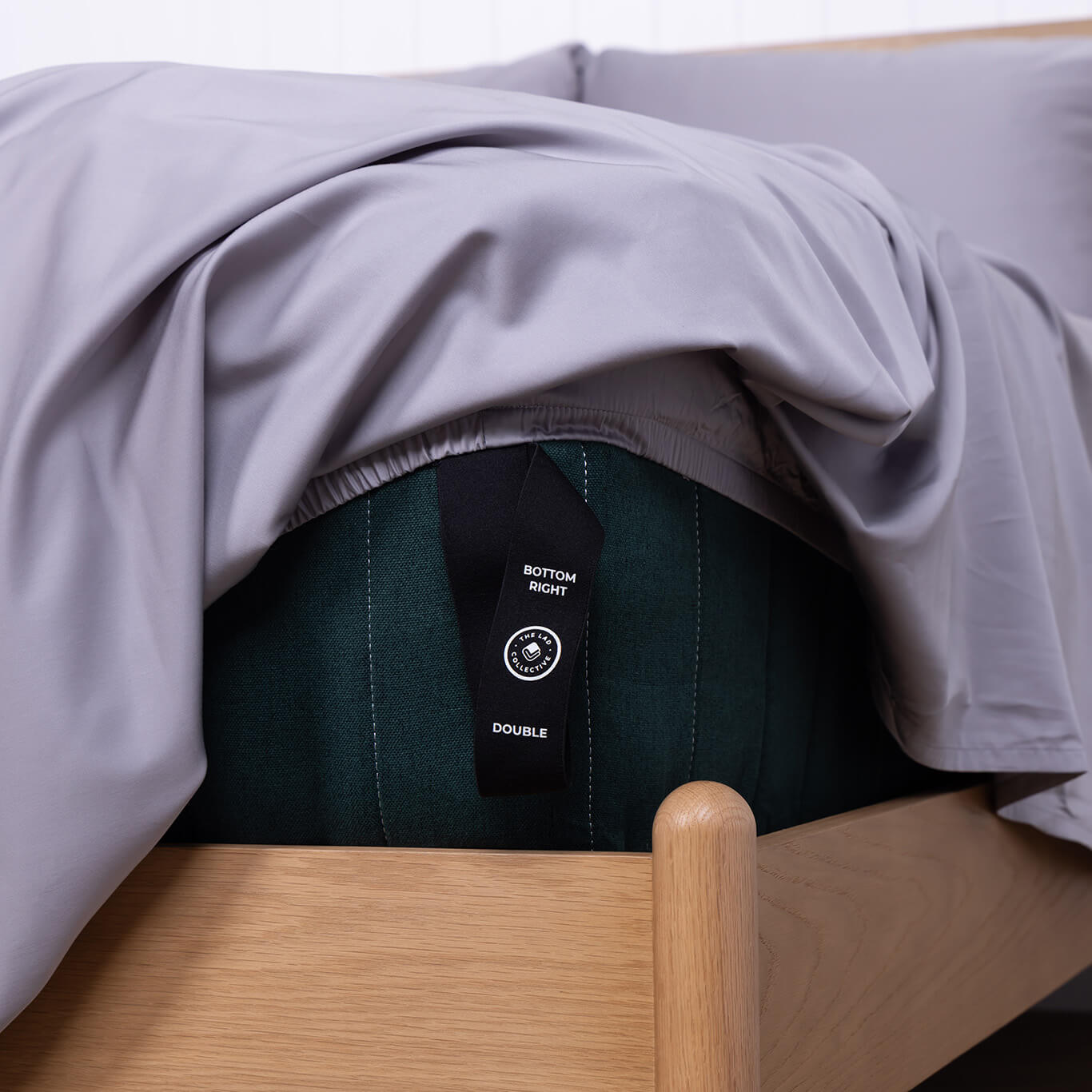 Slate gray fitted sheet with a labeled loop corner strap handing off the side of a bed.