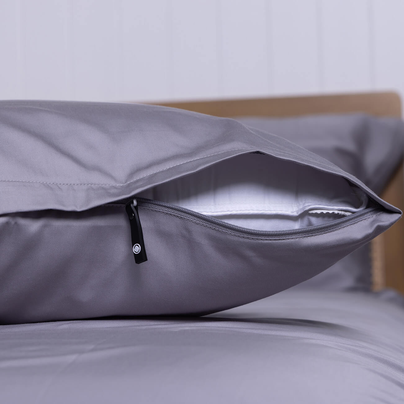 Slate gray pillow with zipper on a bed.