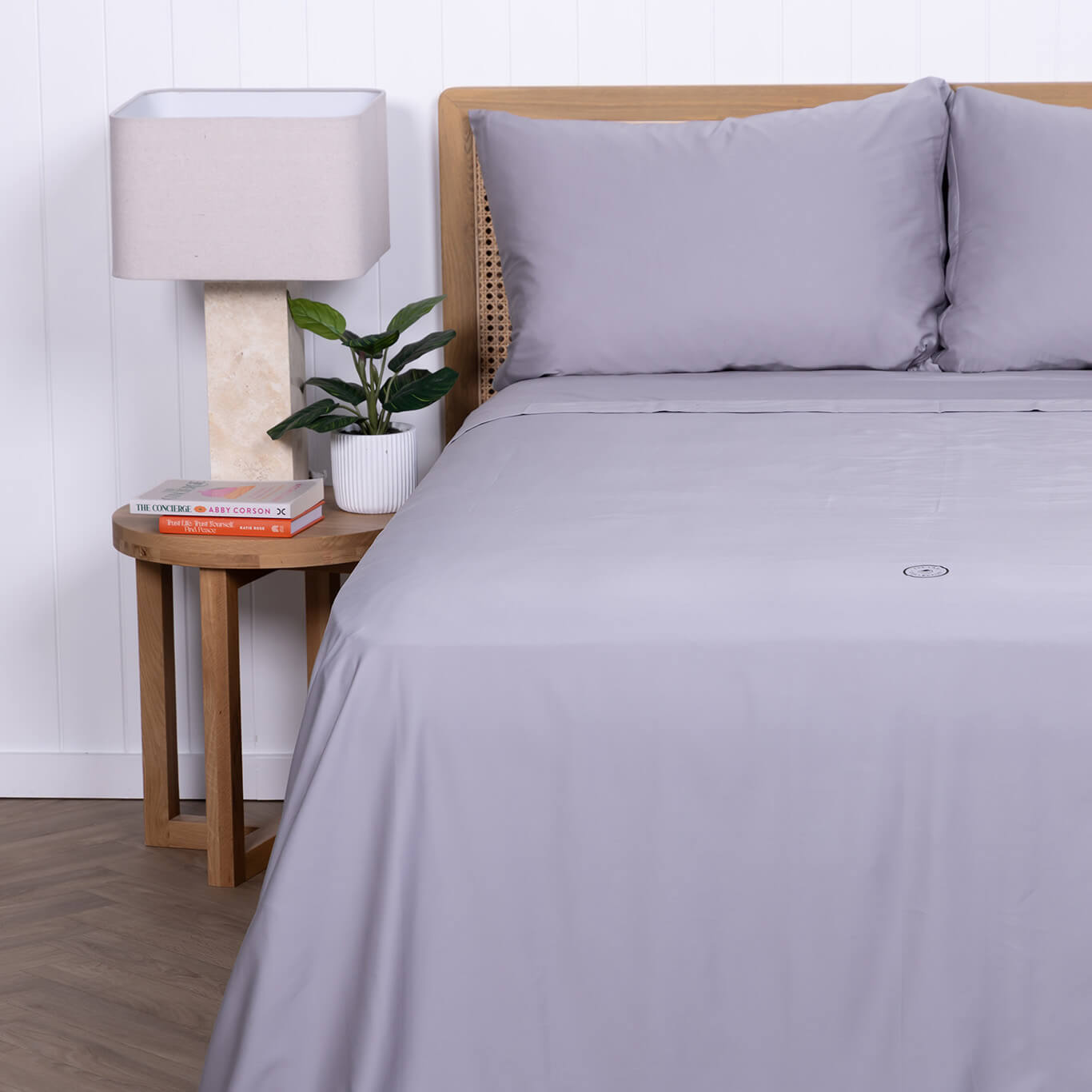 Gray bedding set on a bed with a wooden headboard, nightstand, and lamp.