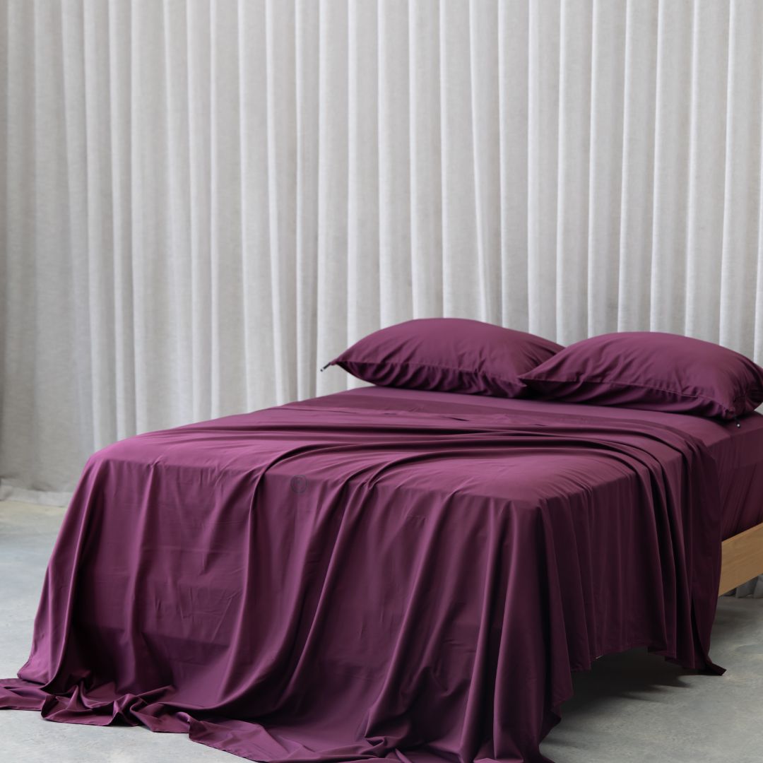 Purple bedspread and pillows on a bed against a white wall