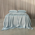 Light blue bedspread on a bed with beige curtains in the background.
