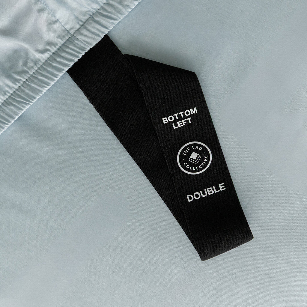 Labelled corner loop strap on light blue fitted sheet.