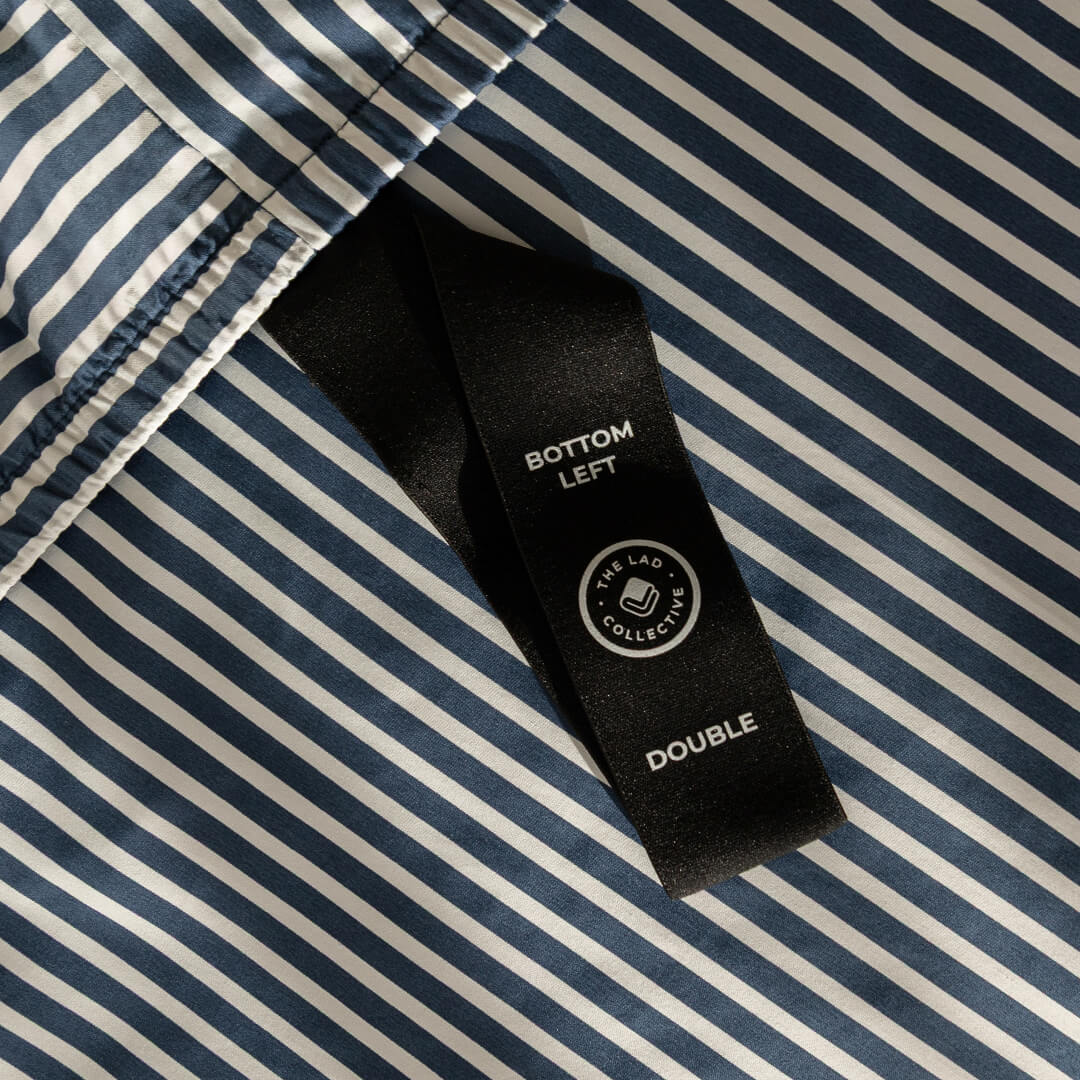 Navy and white pinstripe fitted sheet showcasing labeled corner loop strap.