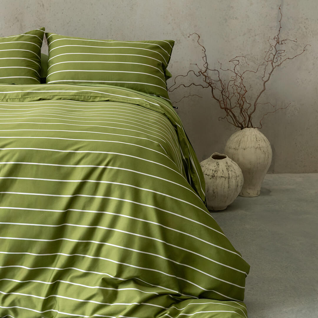 Green striped bedding set on a bed with decorative vases in the background.