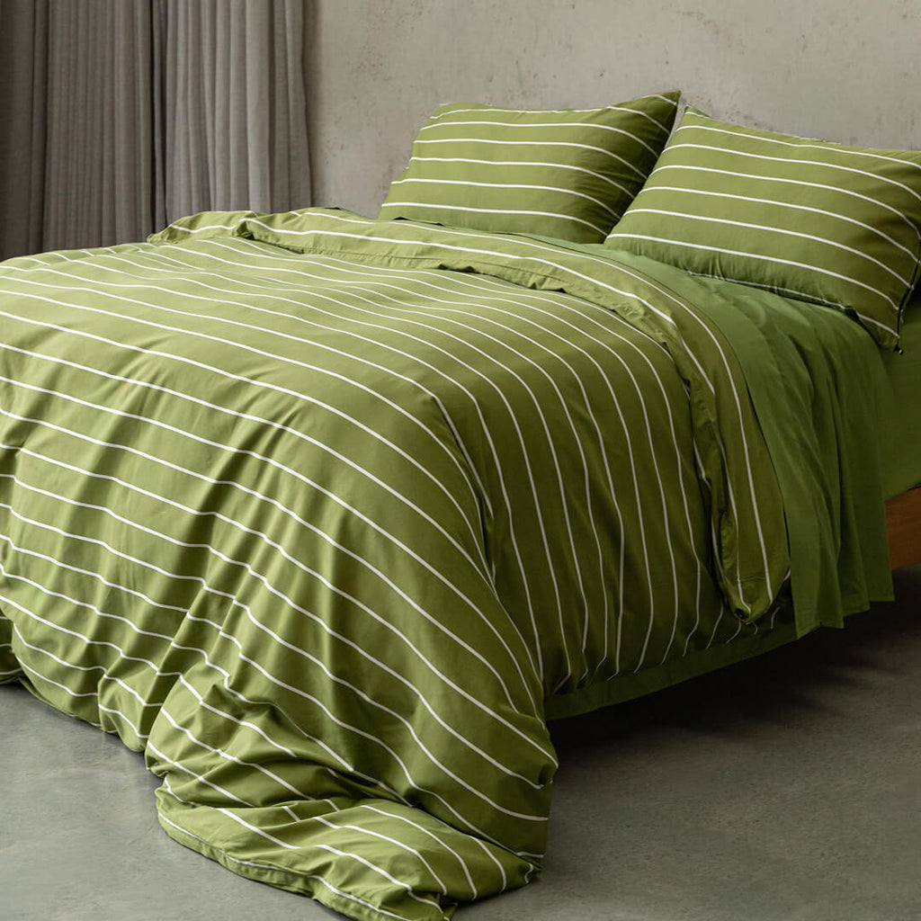 Green striped bedding set on a bed in a room with gray walls and curtains.