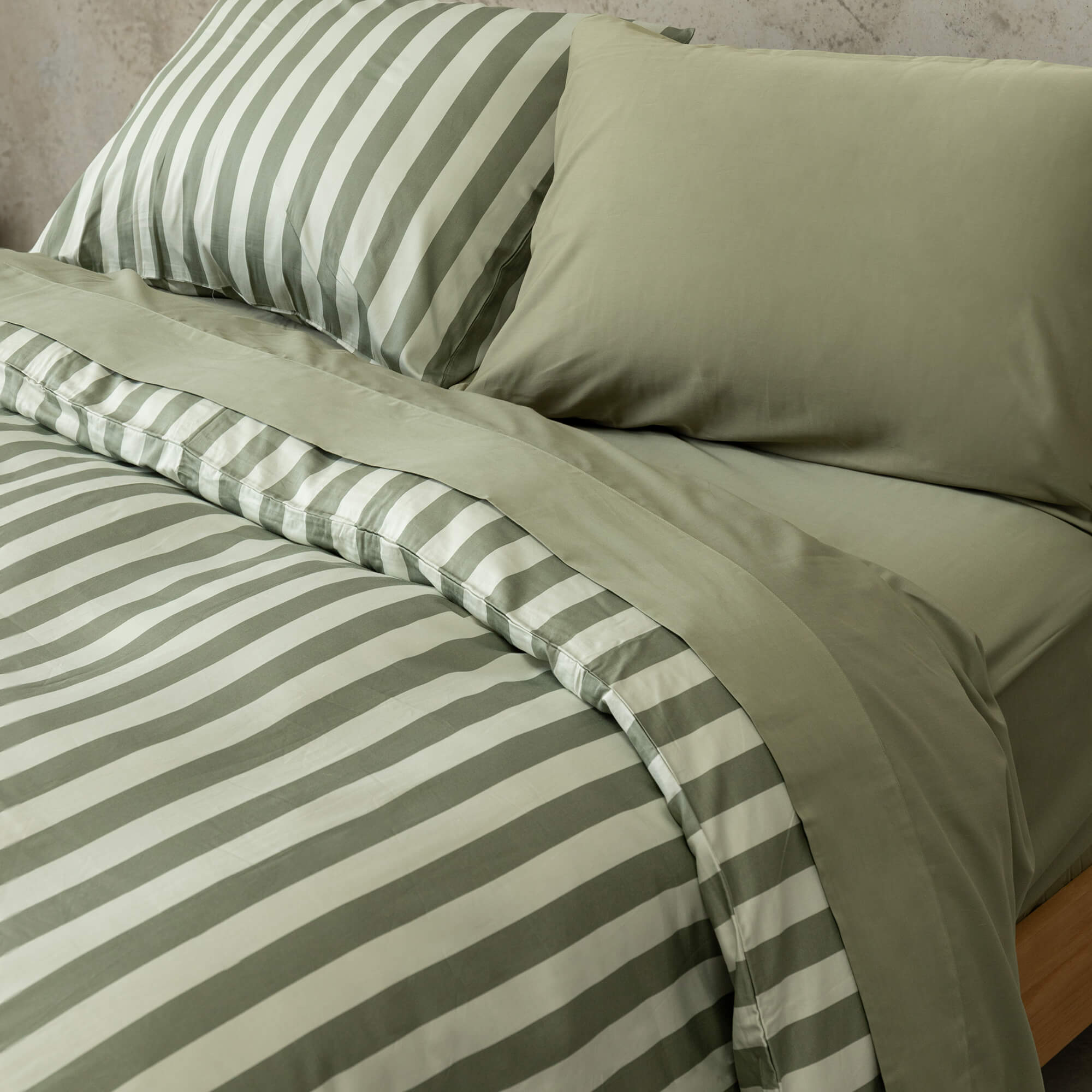 Close up of a sage green and light green stripe duvet cover set on a bed, with sage green sheets and pillowcases.