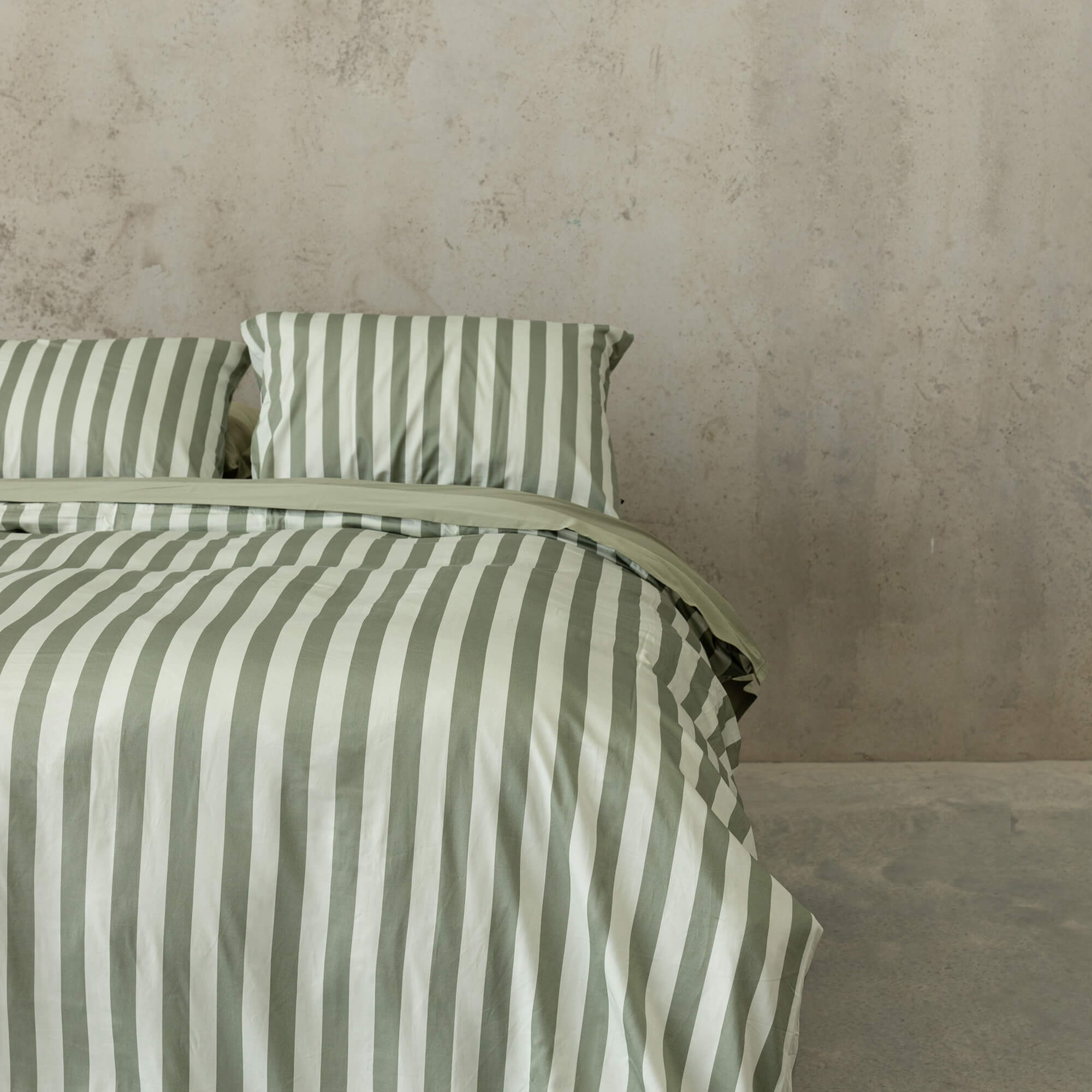 Close up of a sage green and light green stripe duvet cover set on a bed, with sage green sheets and pillowcases.