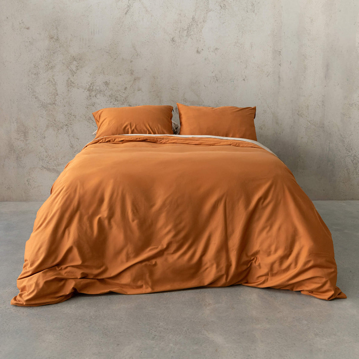 Burnt orange duvet cover set on a bed, against a neutral concrete look backdrop. 