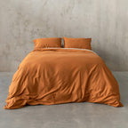 Burnt orange duvet cover set on a bed, against a neutral concrete look backdrop. 